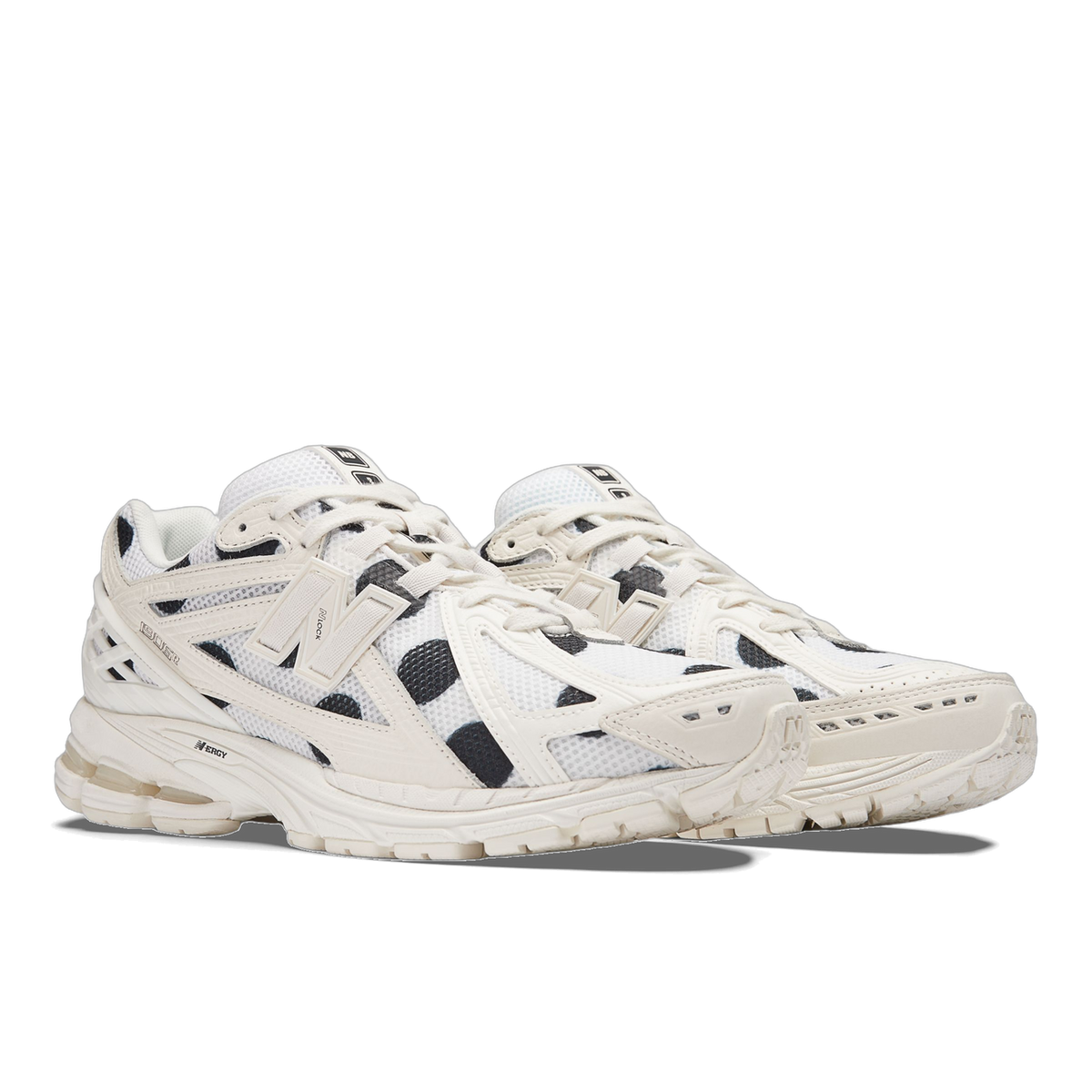 Pair of New Balance 1906R sneakers in white with black polka dot panels and off-white N logo, shown at an angled three-quarter view.