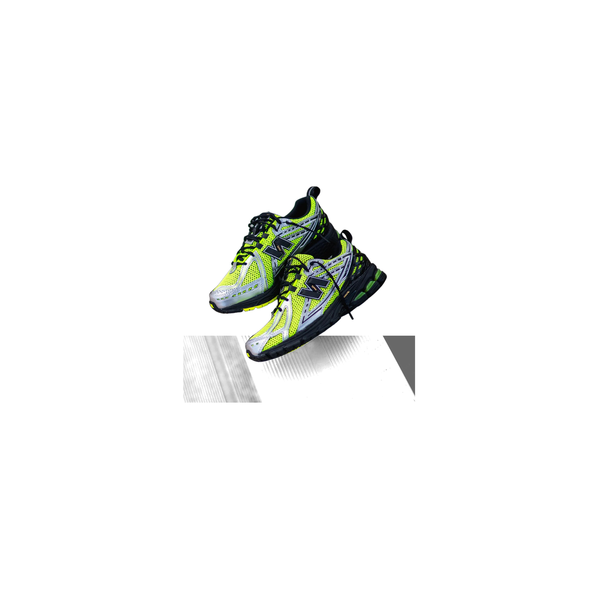 Pair of New Balance 1906R sneakers in volt yellow with black and silver accents, shown resting on a corrugated metal surface over wooden decking.
