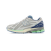 Side view of a gray New Balance 1906R sneaker with navy blue heel accent, light blue N logo, green midsole detailing, and cream outsole.