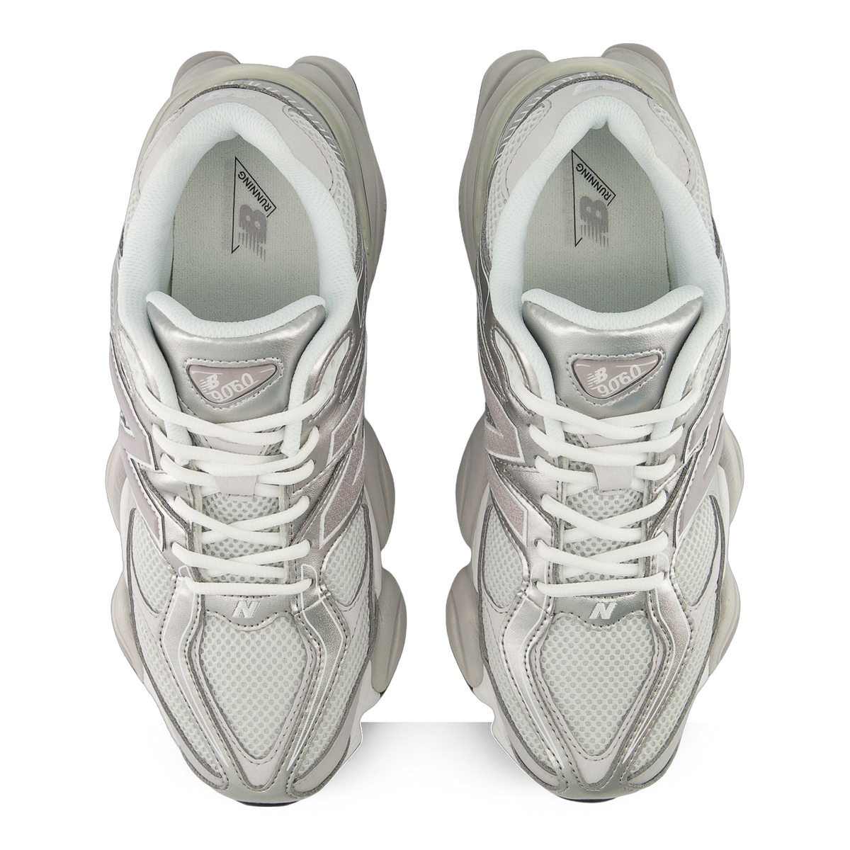 Top-down view of a pair of grey and white New Balance 9060 sneakers with mesh panels, silver overlays, white laces, and visible open tongues showing the branded insoles.