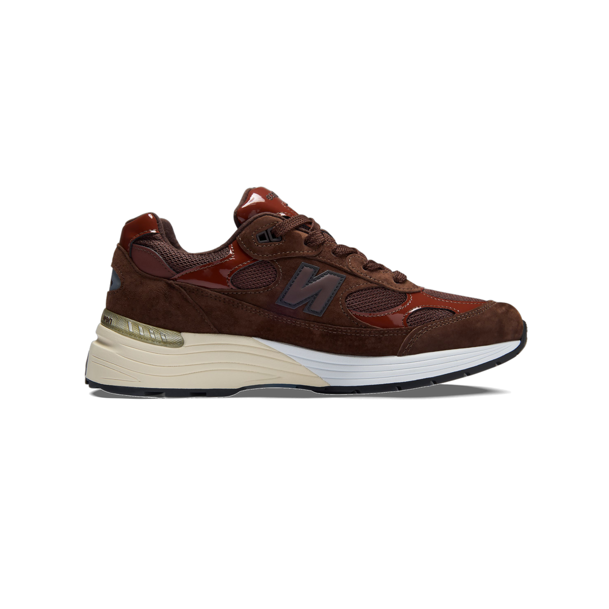 Left brown and rust New Balance 992 sneaker shown from the side with toe pointing left, featuring a mesh and suede upper, patent leather accents, and a cream and white midsole with the N logo.