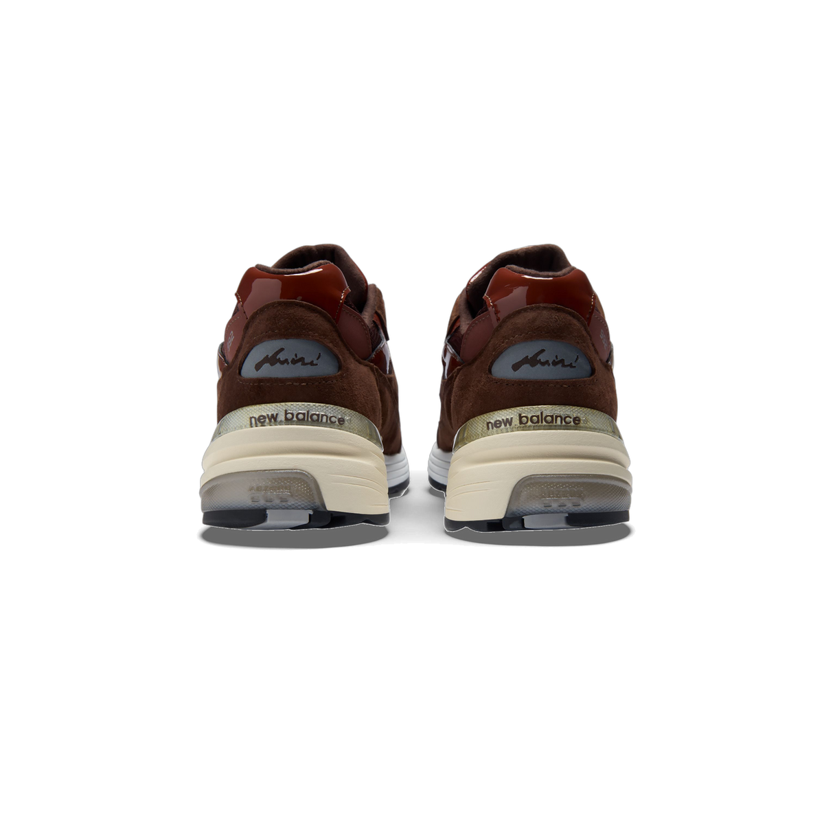 Rear view of a pair of brown suede New Balance 992 sneakers with glossy maroon heel panels, cream midsoles, and a signature logo patch above the heel.