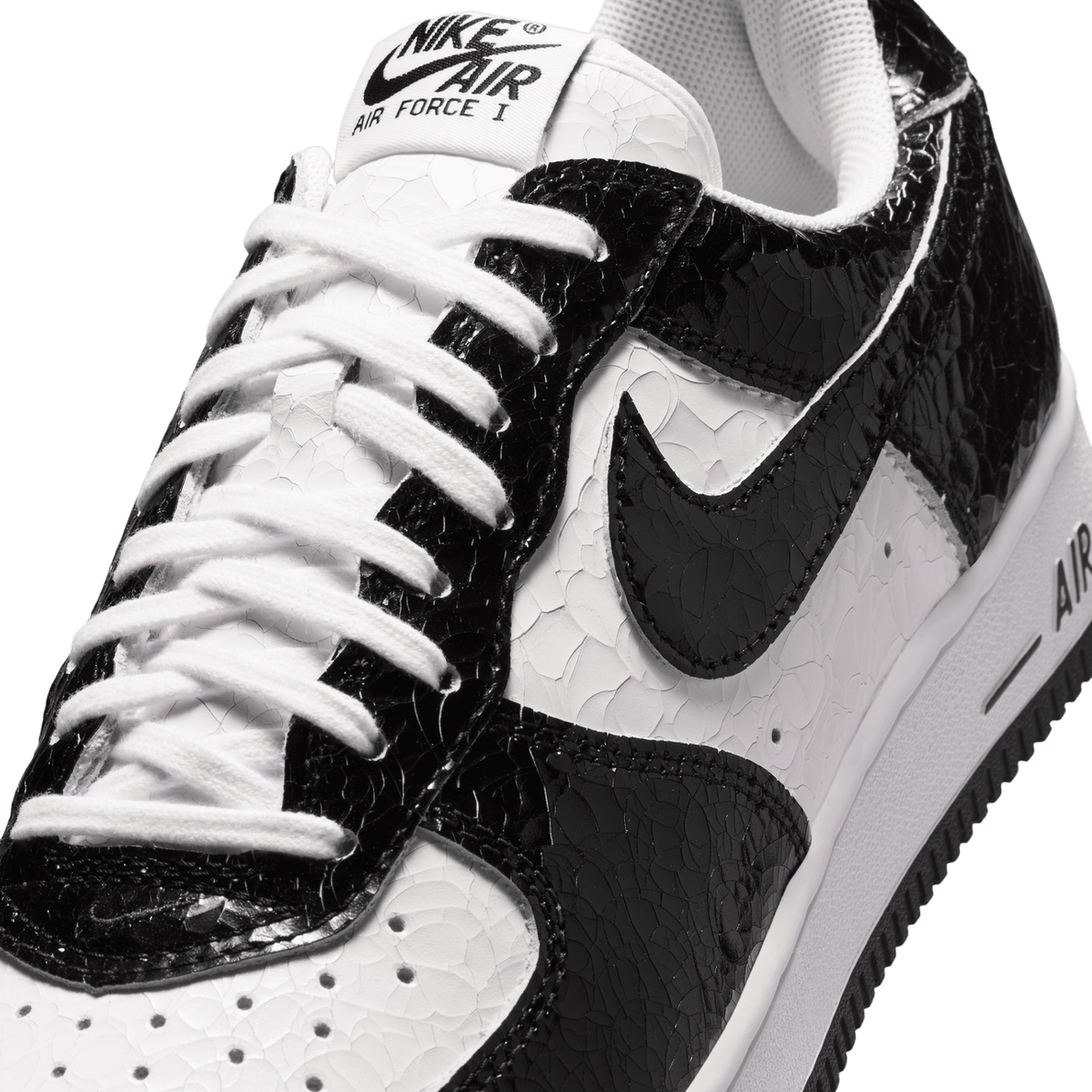 Close-up angled view of a black and white Nike Air Force 1 showing the cracked leather texture, black Swoosh, white laces, and Air Force I tongue branding.