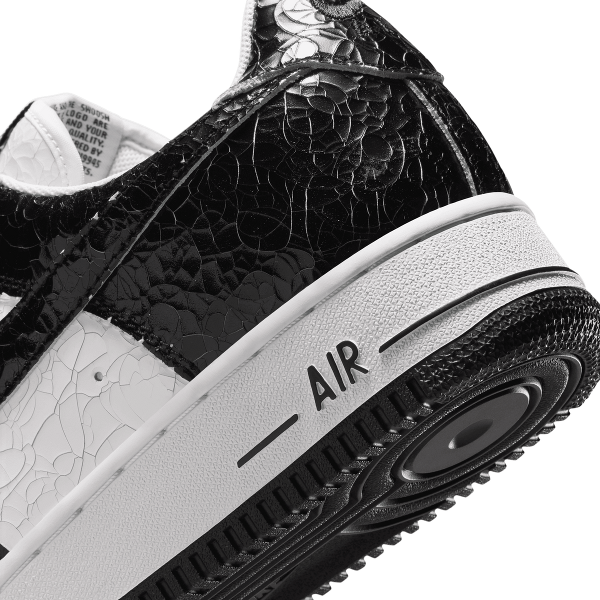 Close-up angled view of a black and white Nike Air Force 1 showing the cracked leather texture on the heel and the 'AIR' branding on the midsole foxing tape.