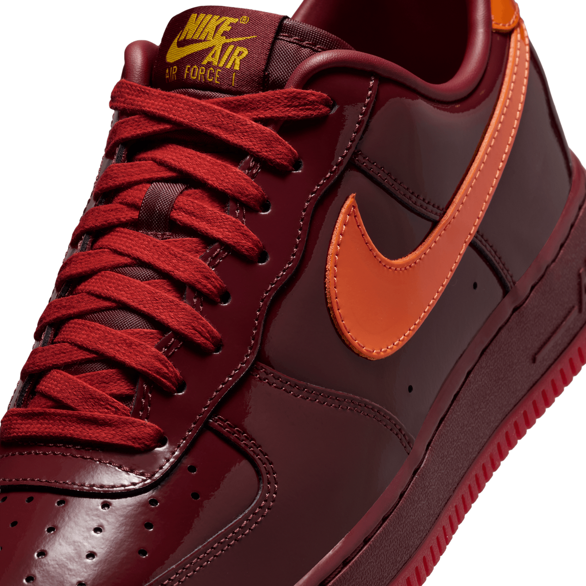 Close-up view of a dark red patent leather Nike Air Force 1 with an orange swoosh, red laces, and Nike Air Force 1 branded tongue tag.