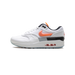 Left Nike Air Max 1 '87 sneaker in white with an orange glowing swoosh, black heel panel, and visible Air unit in the midsole, toe pointing left