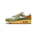 A single green, white, and orange Nike Air Max 1 sneaker viewed from the outside, toe pointing left, showing the white Swoosh logo on the green upper and the yellow Air Max sole with a visible Air unit.