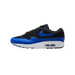 Single black and royal blue Nike Air Max 1 shoe in side profile, toe pointing left, showing the blue Swoosh on the black mesh and suede upper, blue leather overlays, and white midsole with a visible Air unit.
