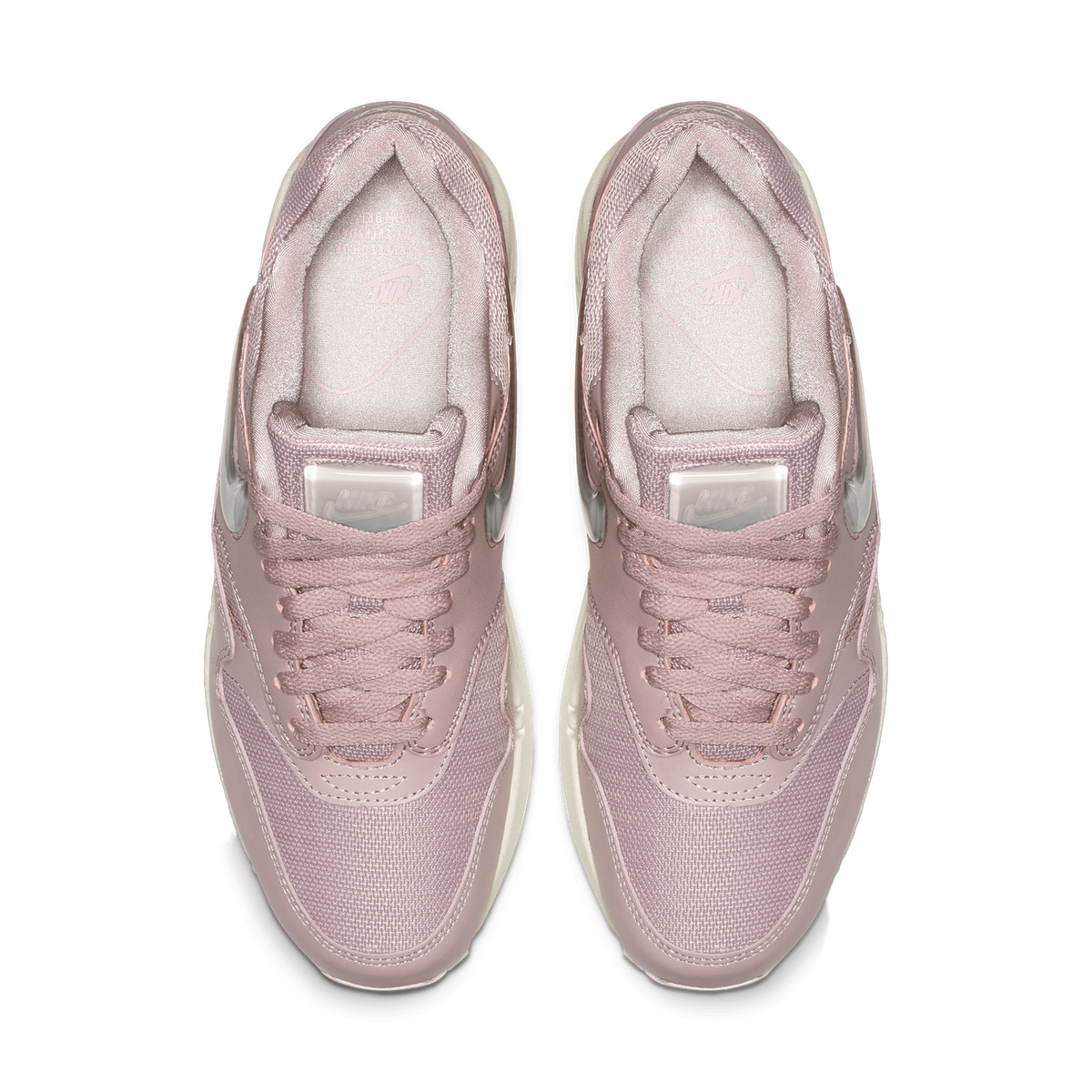 Top-down view of a pair of mauve-pink Nike Air Max 1 sneakers placed side by side, showing the laced tongues, pink interior linings, and the clear translucent Swoosh details along the sides.