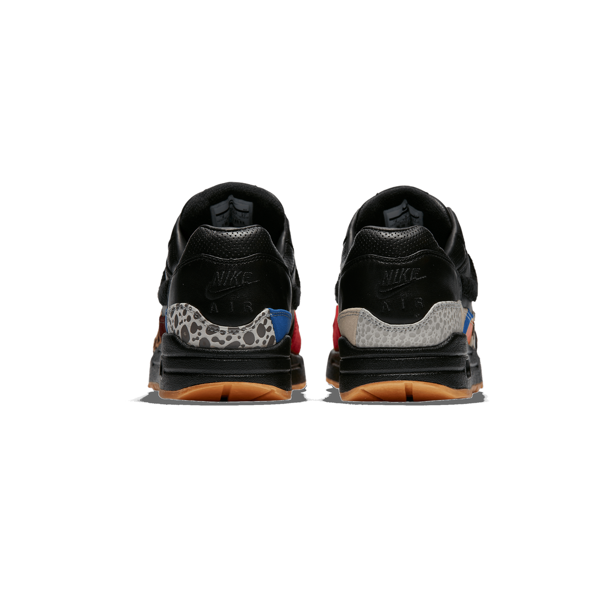 Rear view of a pair of black Nike Air Max 1 sneakers standing side by side, showing the heel tabs with the Nike Swoosh and 'AIR' lettering, multicoloured safari-print panels in grey, red, blue and tan, and gum-coloured outsoles.