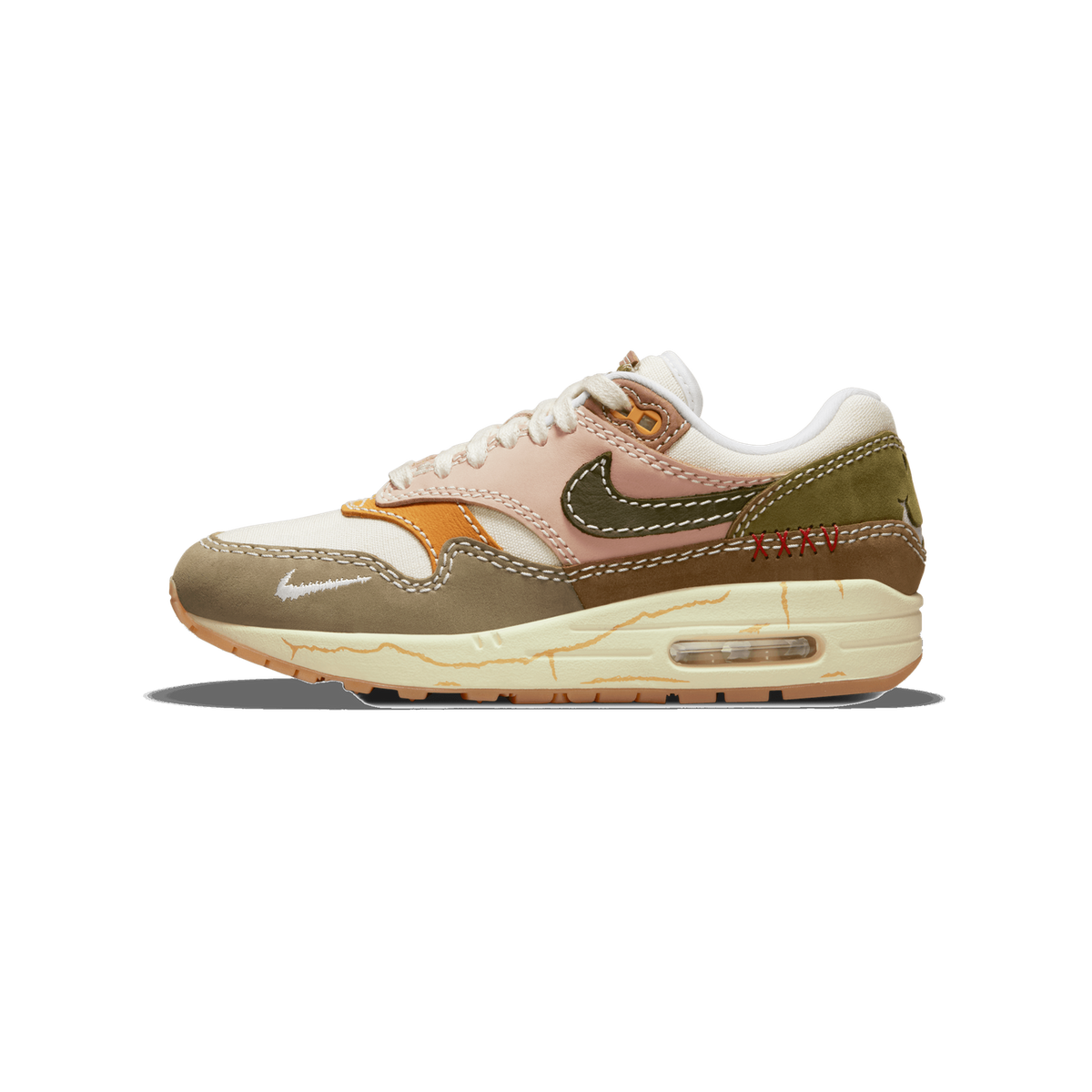 Outside view of a left Nike Air Max 1 sneaker with cream, olive green, pink, orange and brown panels, an olive Swoosh, red cross-stitch detailing, and a crackled cream midsole with visible Air unit.