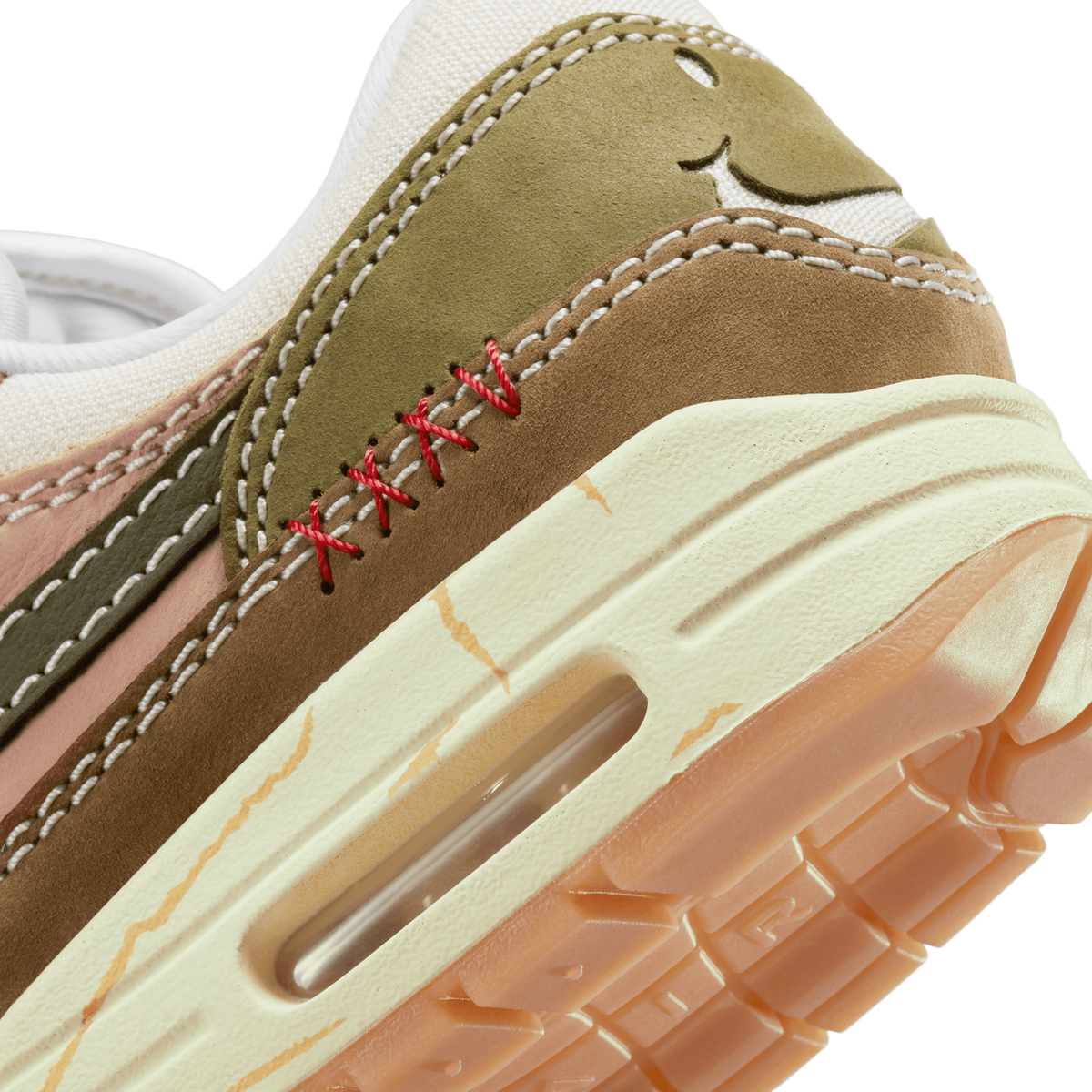 Close-up of the heel and Air unit on a Nike Air Max 1 Premium Wabi-Sabi sneaker, showing olive and brown suede panels with red X-stitching and crackled gold accents above a visible air bubble sole.