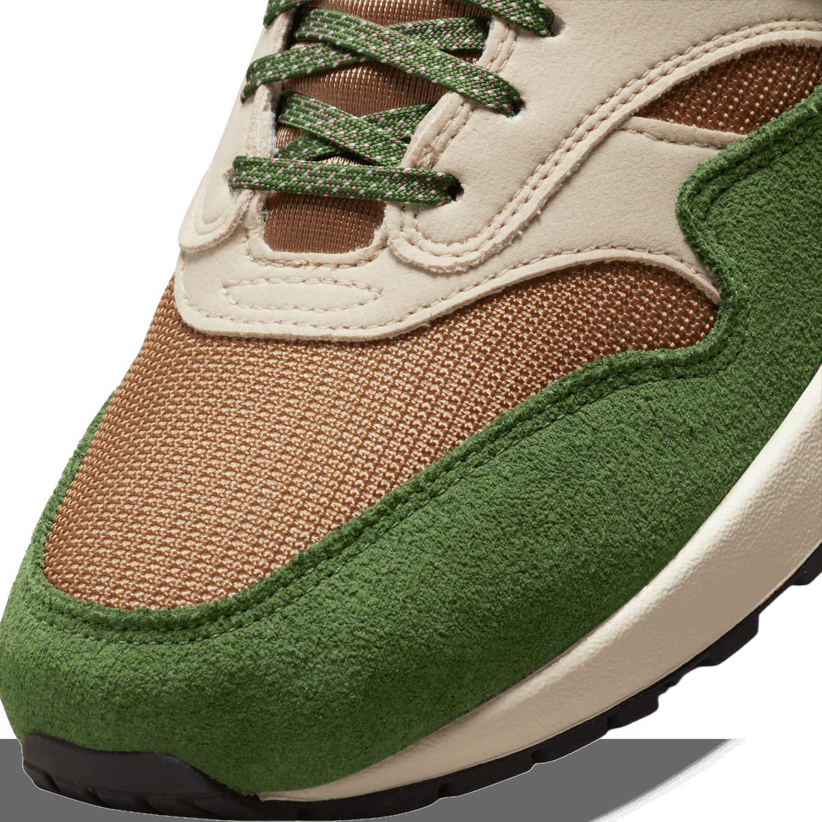 Close-up of a sneaker's toe box showing green suede overlay, tan mesh panel, cream leather trim, and green laces with pink flecks.