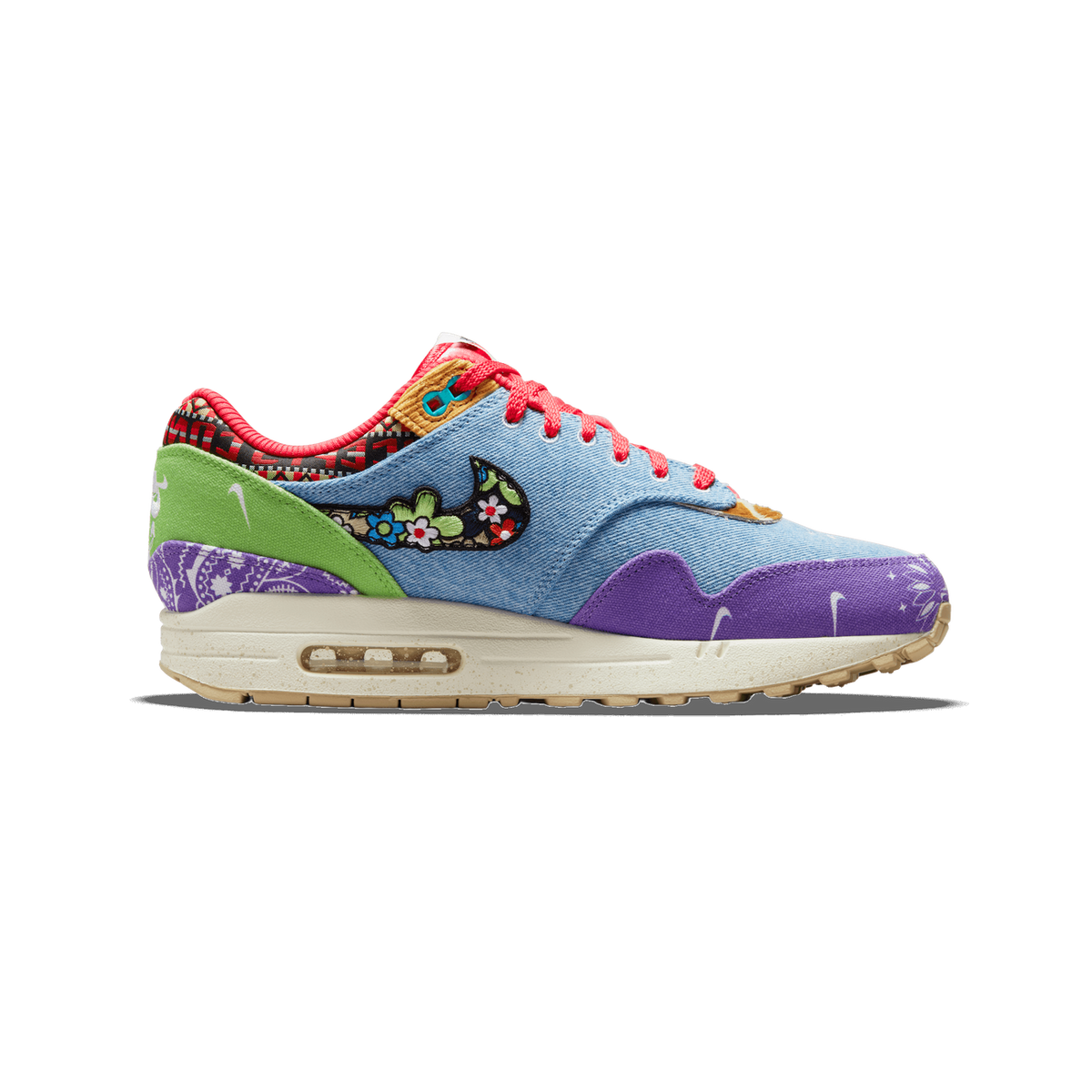 Left Nike Air Max 1 SP sneaker with denim blue upper, floral embroidered swoosh, purple paisley toe and heel, green panel, and red laces, shown from the outside with toe pointing left.