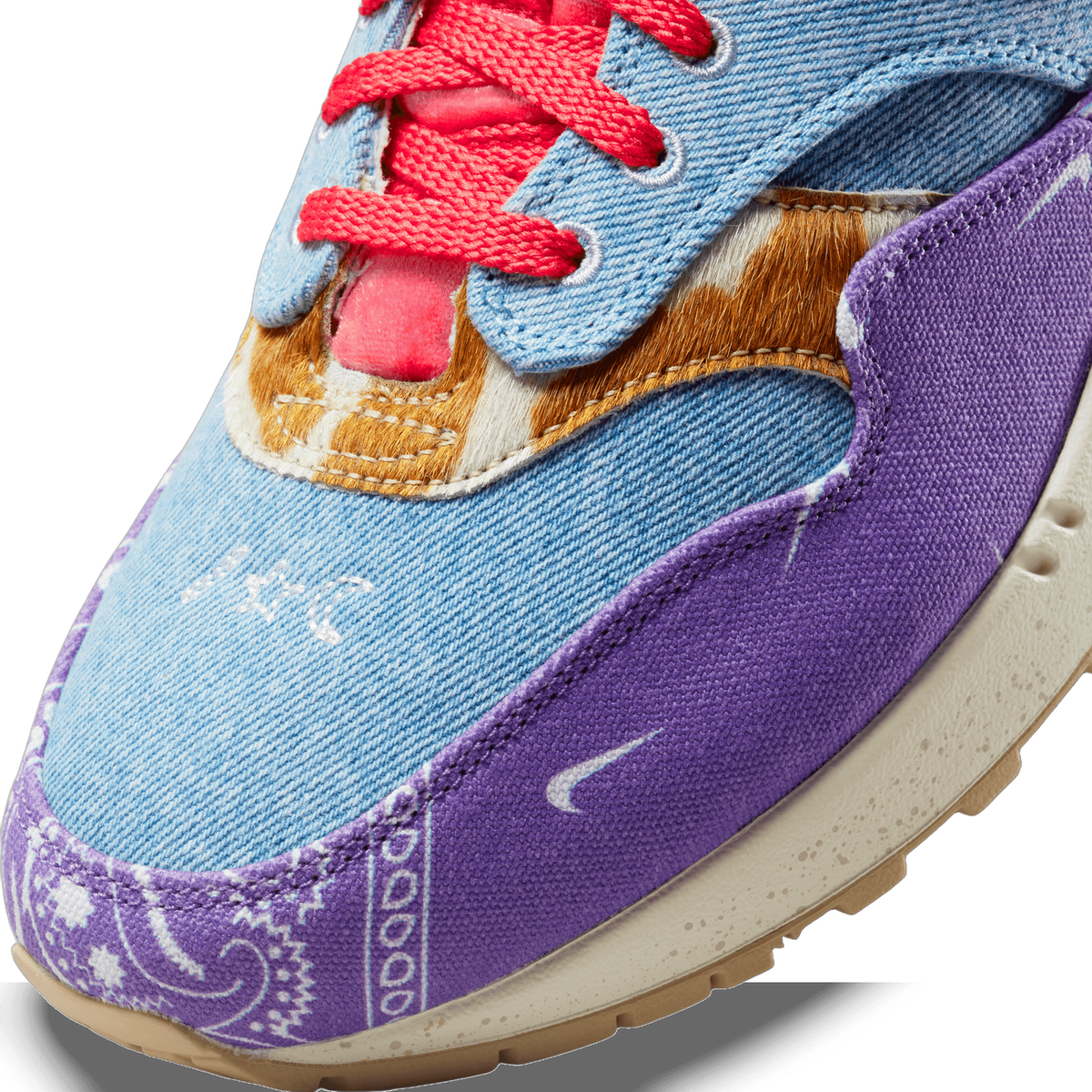 Close-up of the toe box of a Nike Air Max 1 showing denim panels, a purple paisley overlay, faux-fur accent, pink laces, and a small Nike swoosh on the midsole