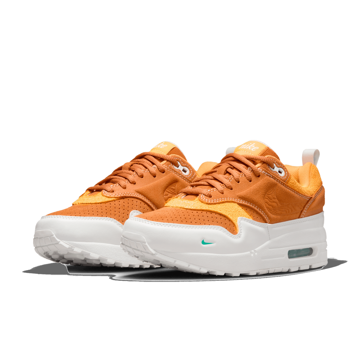 Front-angled view of a pair of orange suede Nike Air Max 1 sneakers with white soles and a small green Nike swoosh on the toe.