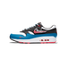 Side profile of a single Nike Air Max 1 sneaker with the toe pointing left, showing a white and black upper with teal-blue accents, red Swoosh and script 'nike' branding on the heel panel, and a visible red and white Air unit in the midsole.