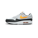 A single white Nike Air Max 1 sneaker shown from the lateral side with the toe pointing left, featuring a gold Swoosh, black suede toe and heel overlays, and a visible clear Air unit in the midsole.