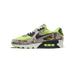 Side view of a Nike Air Max 90 sneaker in green with brown and grey camouflage panels, a black swoosh, and white laces and midsole.