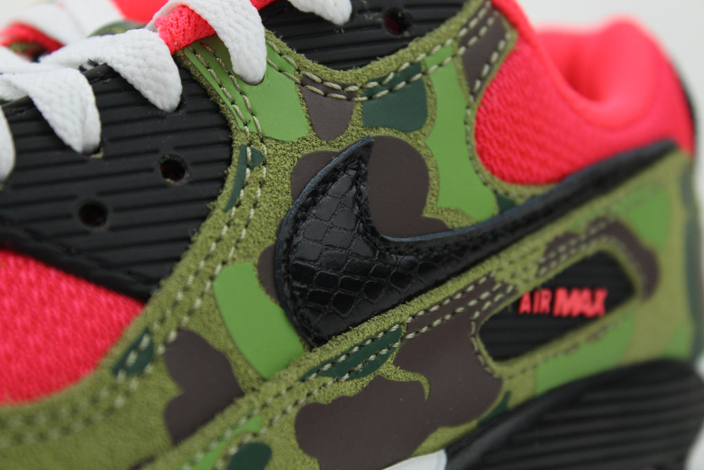 Close-up of Nike Air Max 90 'Reverse Duck Camo' sneaker, featuring bold reverse camo pattern, vibrant color accents, and signature Air cushioning, ideal for fashion-forward sneaker enthusiasts and collectors.