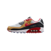 Side view of a white, gold, black and red Nike Air Max 90 sneaker with toe pointing left, showing a red Swoosh and an 'SF' logo patch near the heel, and a visible Air unit in the midsole