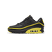 Side view of a black Nike Air Max 90 Undefeated sneaker with yellow piping, swoosh outline, and visible air unit in the yellow midsole, toe pointing left