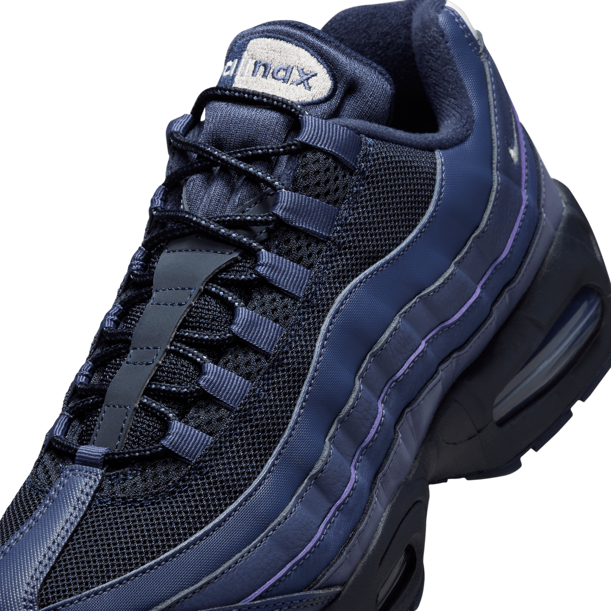 Close-up angled view of a navy and black Nike Air Max 95 showing the mesh upper, navy laces with tongue tab, the beige Air Max tongue label, and purple accent stitching along the midfoot overlay.
