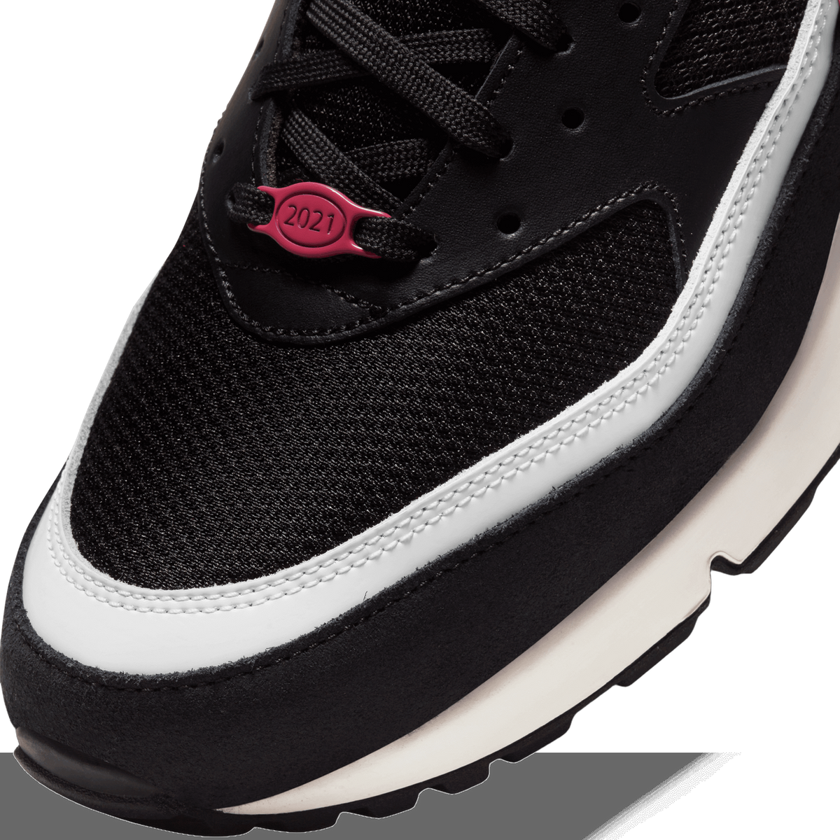 Close-up of a black Nike sneaker's toe box showing a pink lace toggle marked 2021, white midsole trim, and black laces.