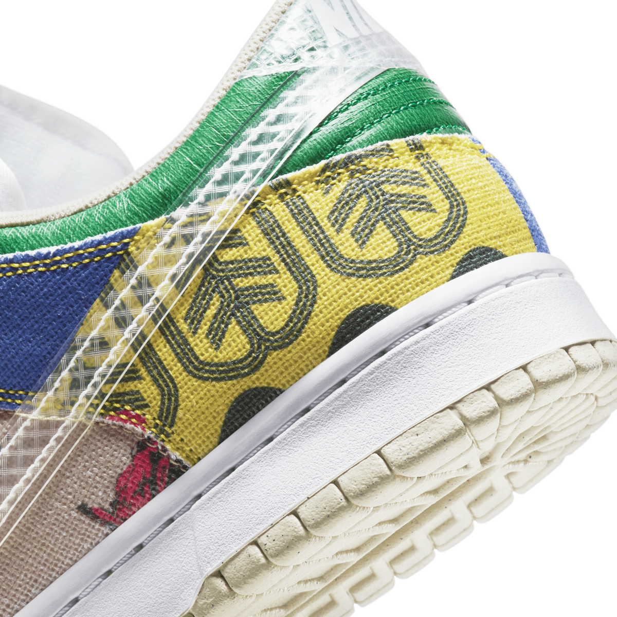 Close-up view of a Nike Dunk Low City Market sneaker showing patterned yellow fabric with dark logo print, green and blue panels, and a cream textured outsole.