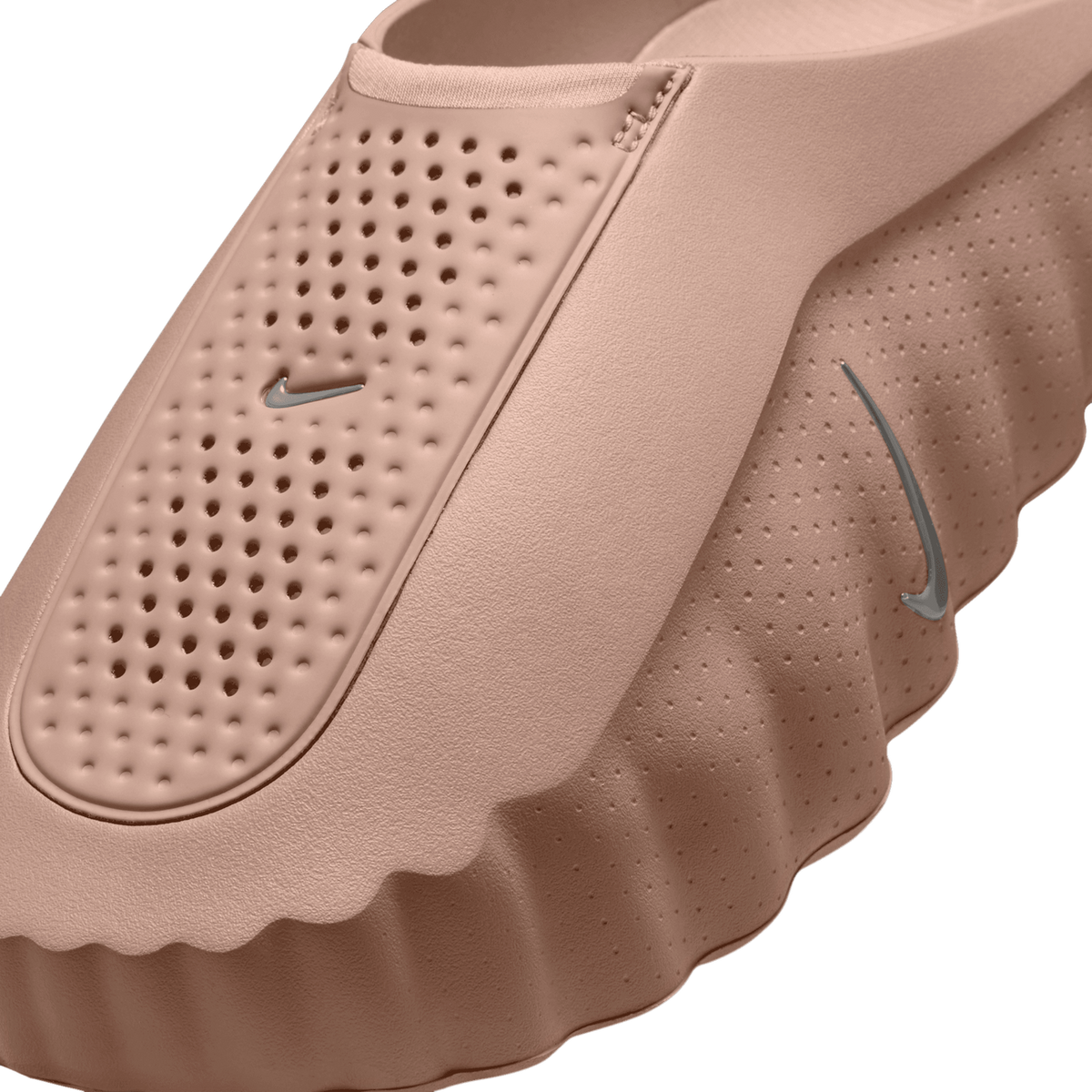 Close-up angled view of a tan perforated slip-on shoe showing the insole, Nike swoosh logos, and ruffled midsole texture.