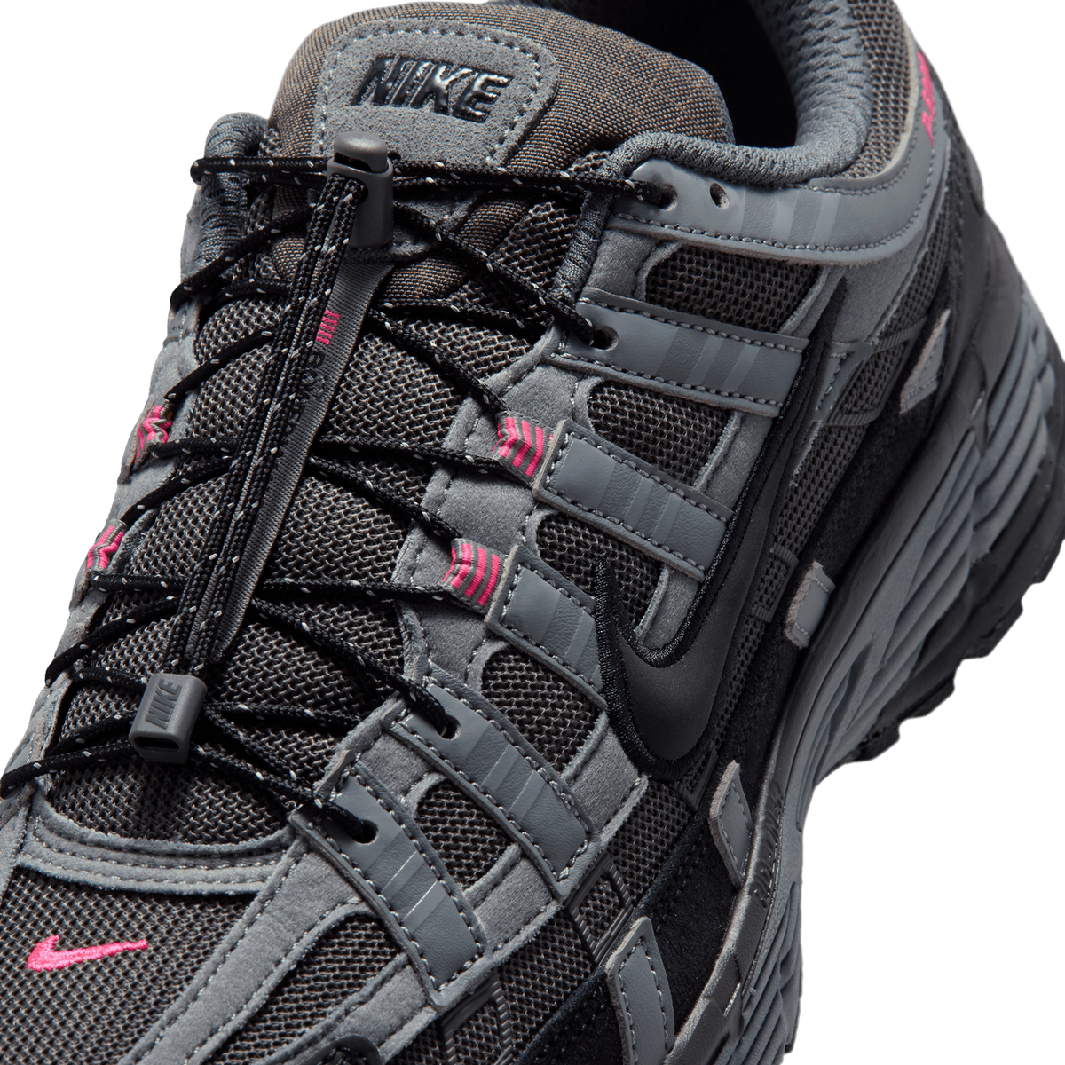 Close-up of a black and grey Nike P-6000 sneaker showing the lacing system with black elastic laces and grey cord lock, the tongue with a Nike logo, pink accents on the eyelet straps, and the black Swoosh on the side panel.