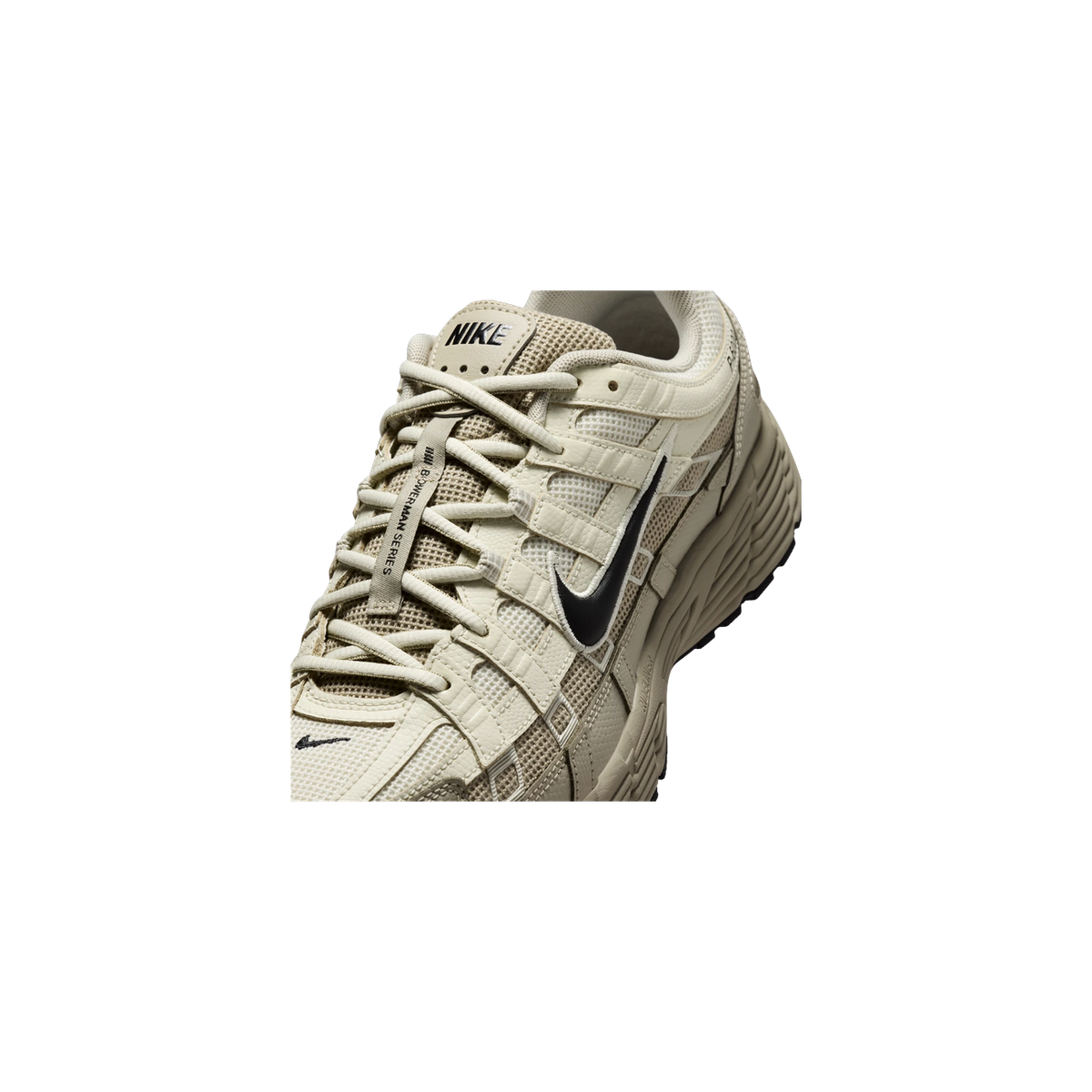 Close-up angled view of a beige Nike P-6000 sneaker showing the laces, tongue with Nike logo, and layered mesh and leather panels with a black swoosh.