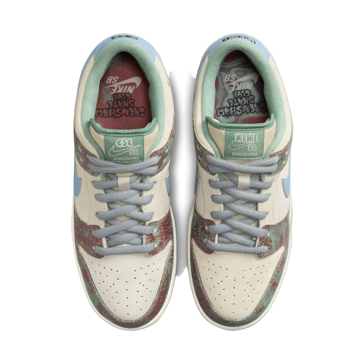 Top-down view of a pair of Nike SB Dunk Low sneakers placed side by side, showing the cream suede uppers with red and green textured overlays, light blue Swoosh logos, grey laces, and the green heel tabs and red-lined insoles visible inside the colla