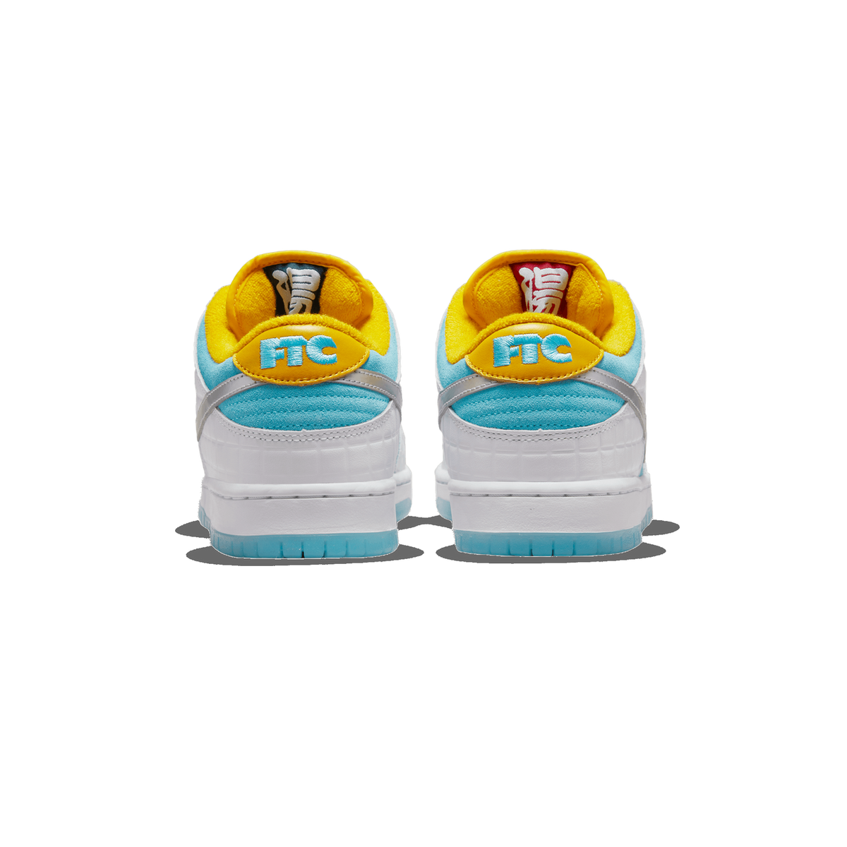 Rear view of a pair of white, light blue, and yellow Nike SB Dunk Low sneakers on a white background, showing the yellow heel tabs embroidered with FTC and the yellow-lined collars with white and red Japanese characters inside.