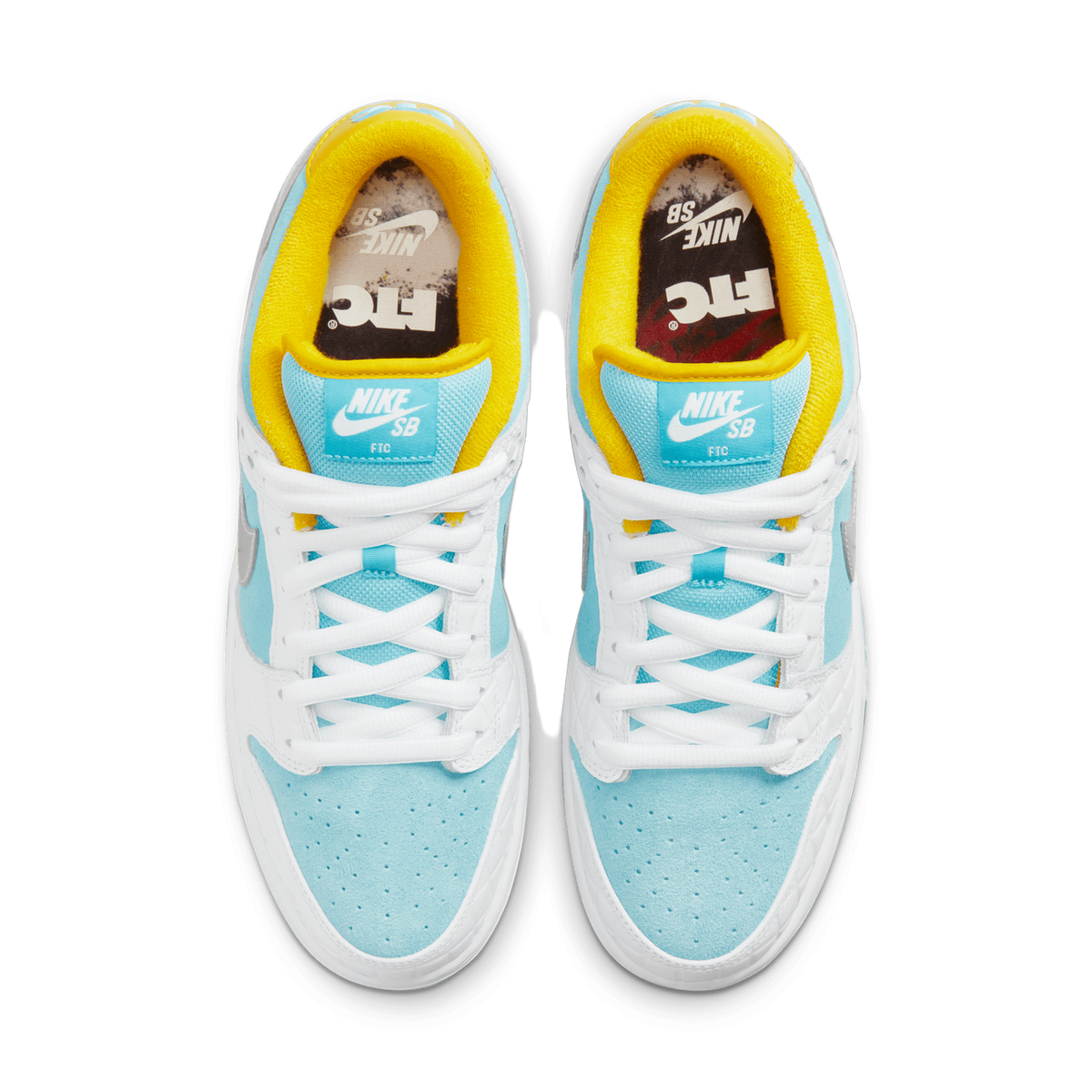 Top-down view of a pair of Nike SB Dunk Low sneakers placed side by side with toes pointing up, showing light blue suede overlays, white leather panels, yellow collar linings, and FTC branded insoles.