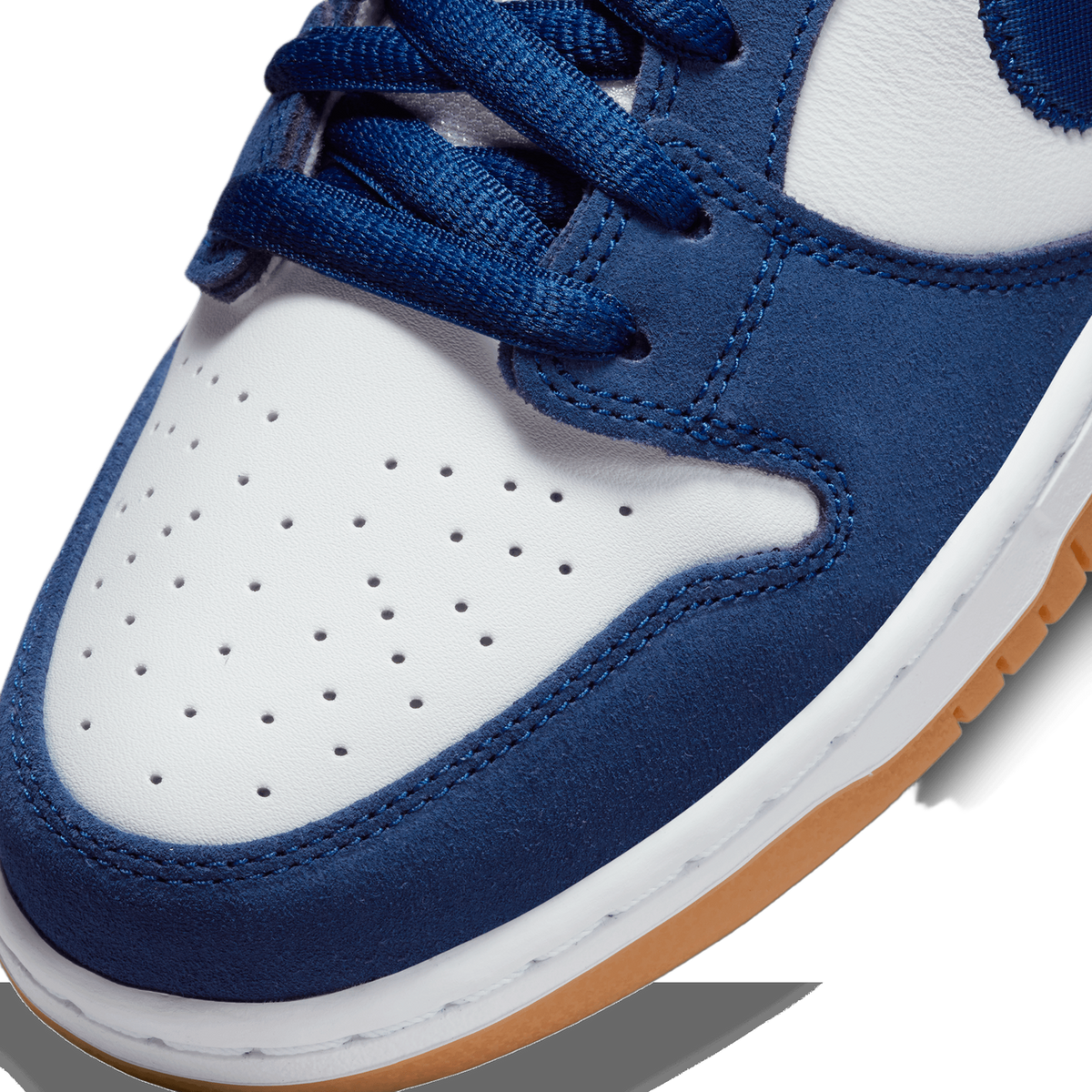Close-up of the toe box of a navy blue and white Nike SB Dunk Low showing suede overlays, perforated toe cap, and gum sole.