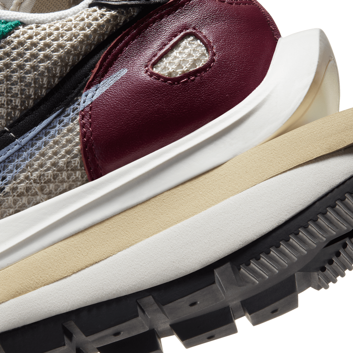 Close-up detail of the heel and midsole of a sneaker showing a burgundy leather heel panel with a stitched cream mesh cutout, a white and tan layered midsole, and a black lugged rubber outsole edge.
