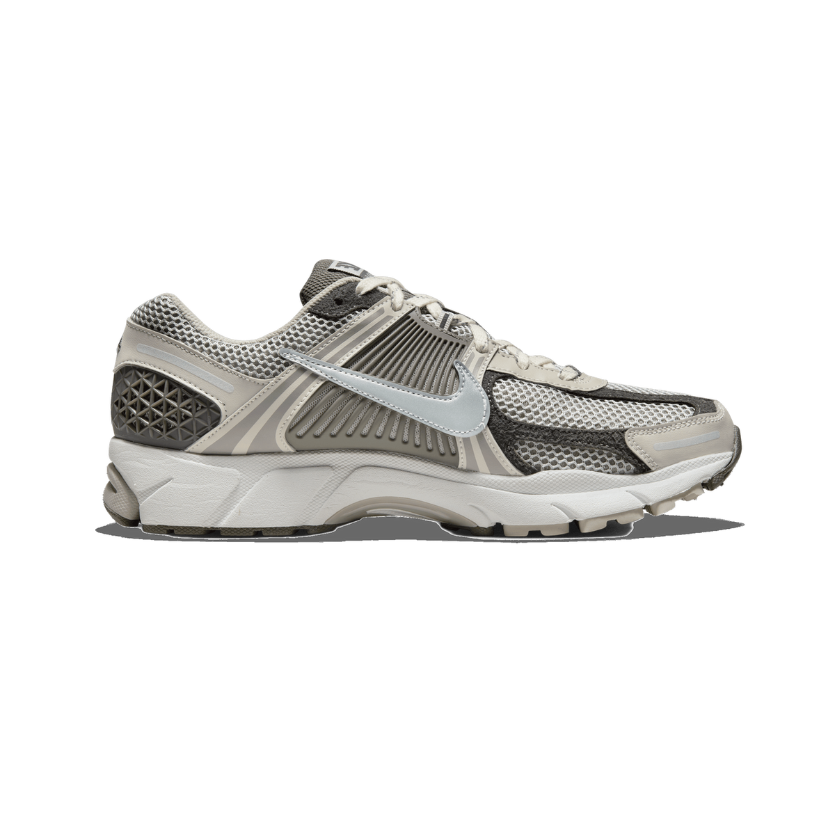 Side profile of a single grey and beige Nike Zoom Vomero 5 sneaker with the toe pointing left, showing a mesh upper with darker grey overlays, a metallic silver Swoosh, and a white midsole with a grey heel pod.