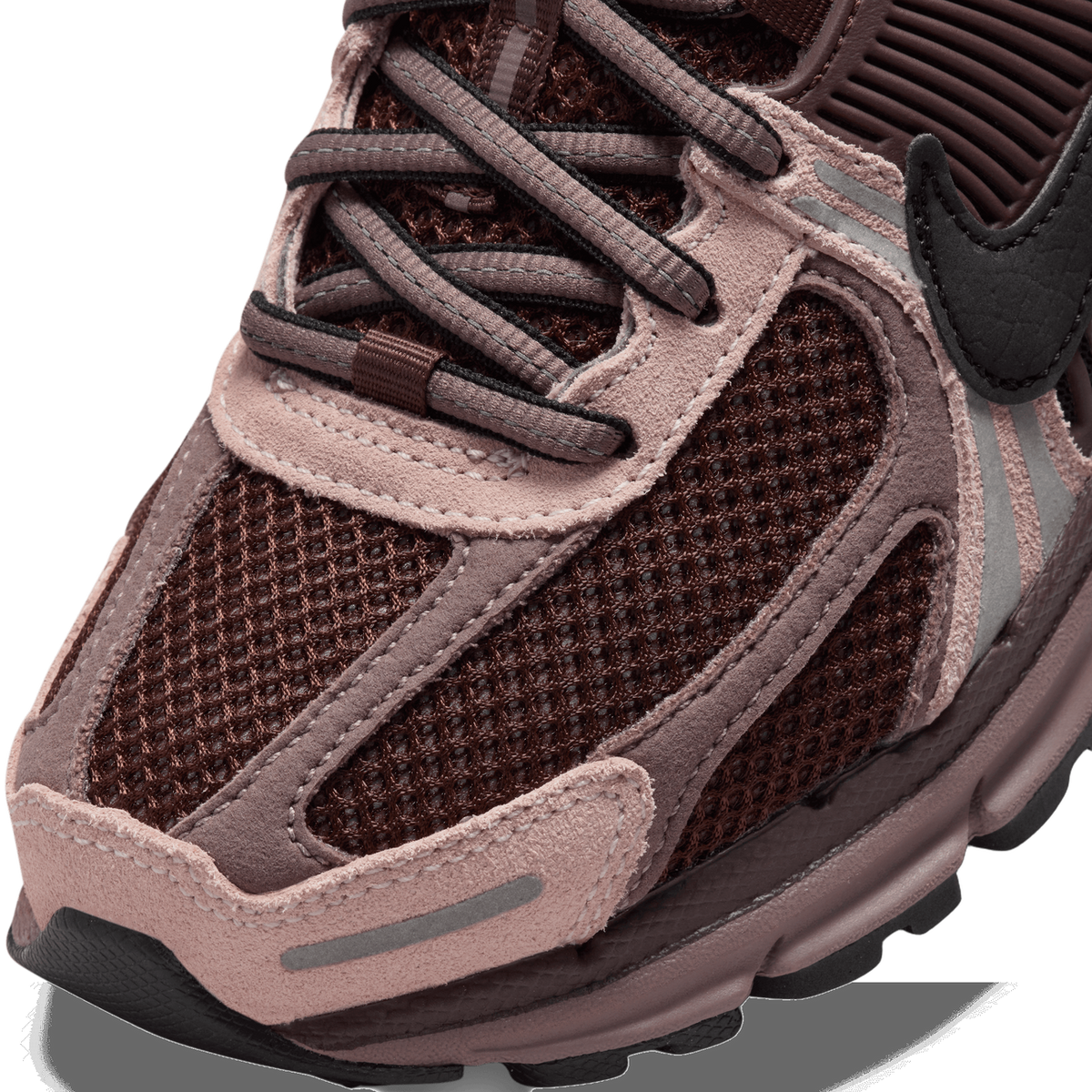 Close-up detail of the toe and lacing area of a brown and mauve Nike sneaker, showing mesh panels, pink suede overlays, a black Swoosh logo, and a reflective strip on the toe.