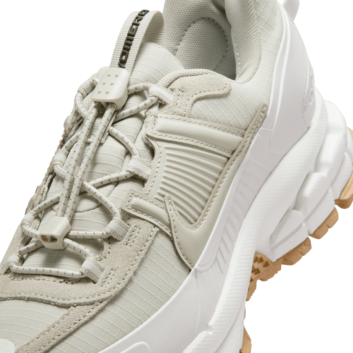 Close-up view of a light stone Nike Zoom Vomero 5 showing the toggle lacing system, textured mudguard panel, and white midsole with gum rubber outsole.