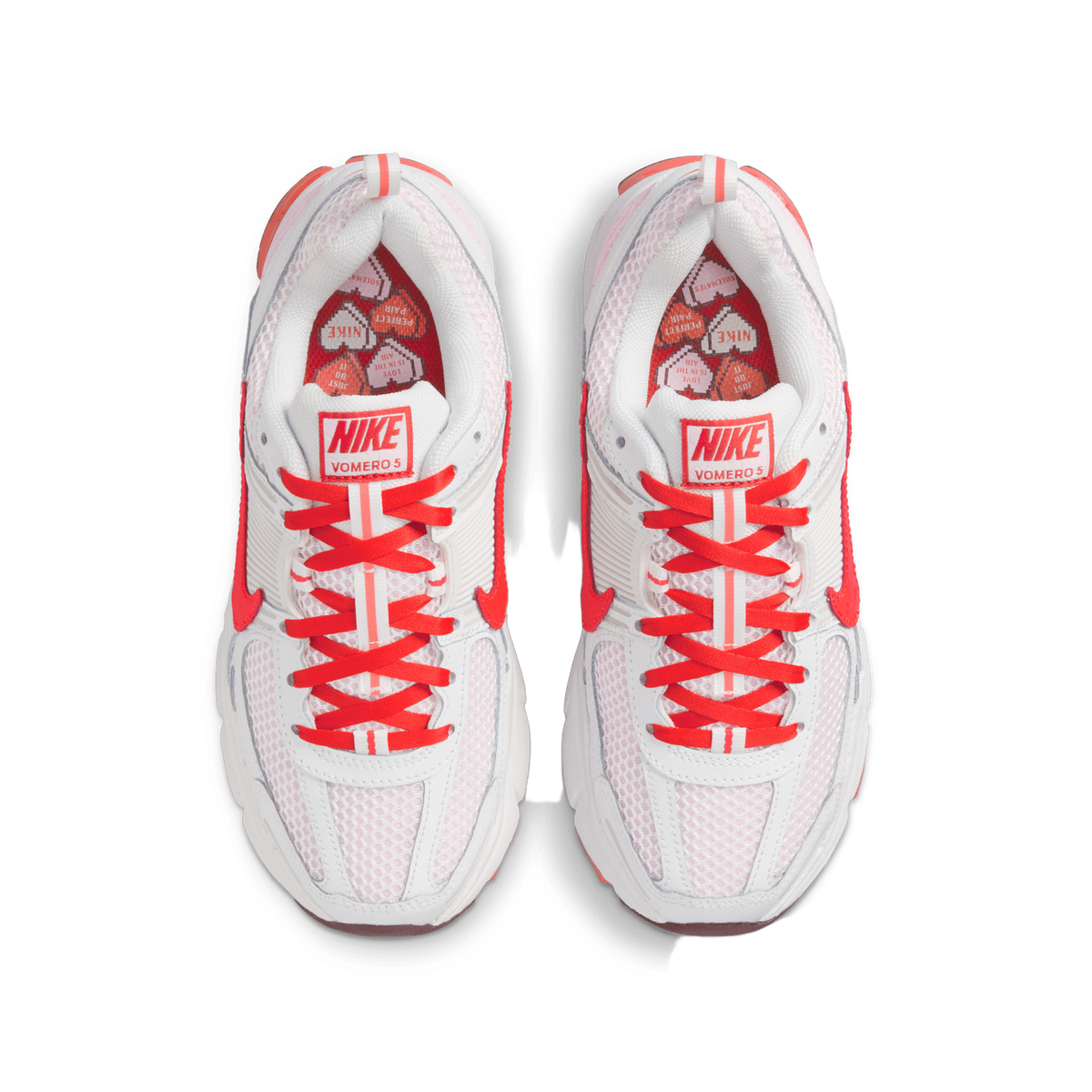 Top-down view of a pair of white Nike Vomero 5 sneakers with red laces and red Swoosh logos, showing the heart-patterned red and pink lining visible inside the collars.