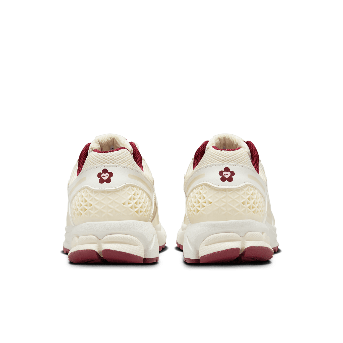Rear view of a pair of cream Nike Zoom Vomero 5 sneakers with dark red heel accents, textured heel panels, and a flower-shaped logo with a heart on each heel