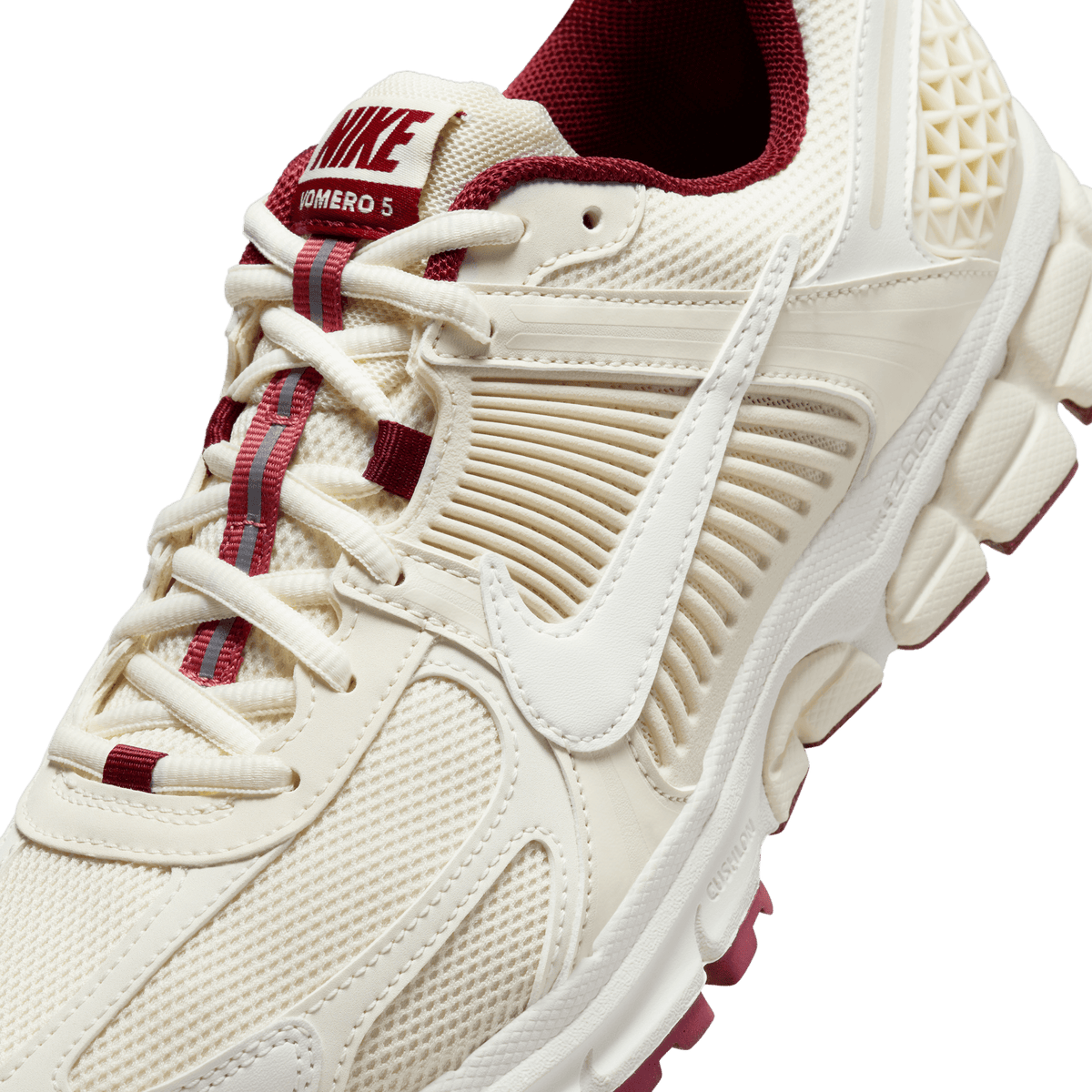 Close-up angled view of a cream Nike Zoom Vomero 5 sneaker with burgundy accents, mesh upper, and Vomero 5 tongue tag