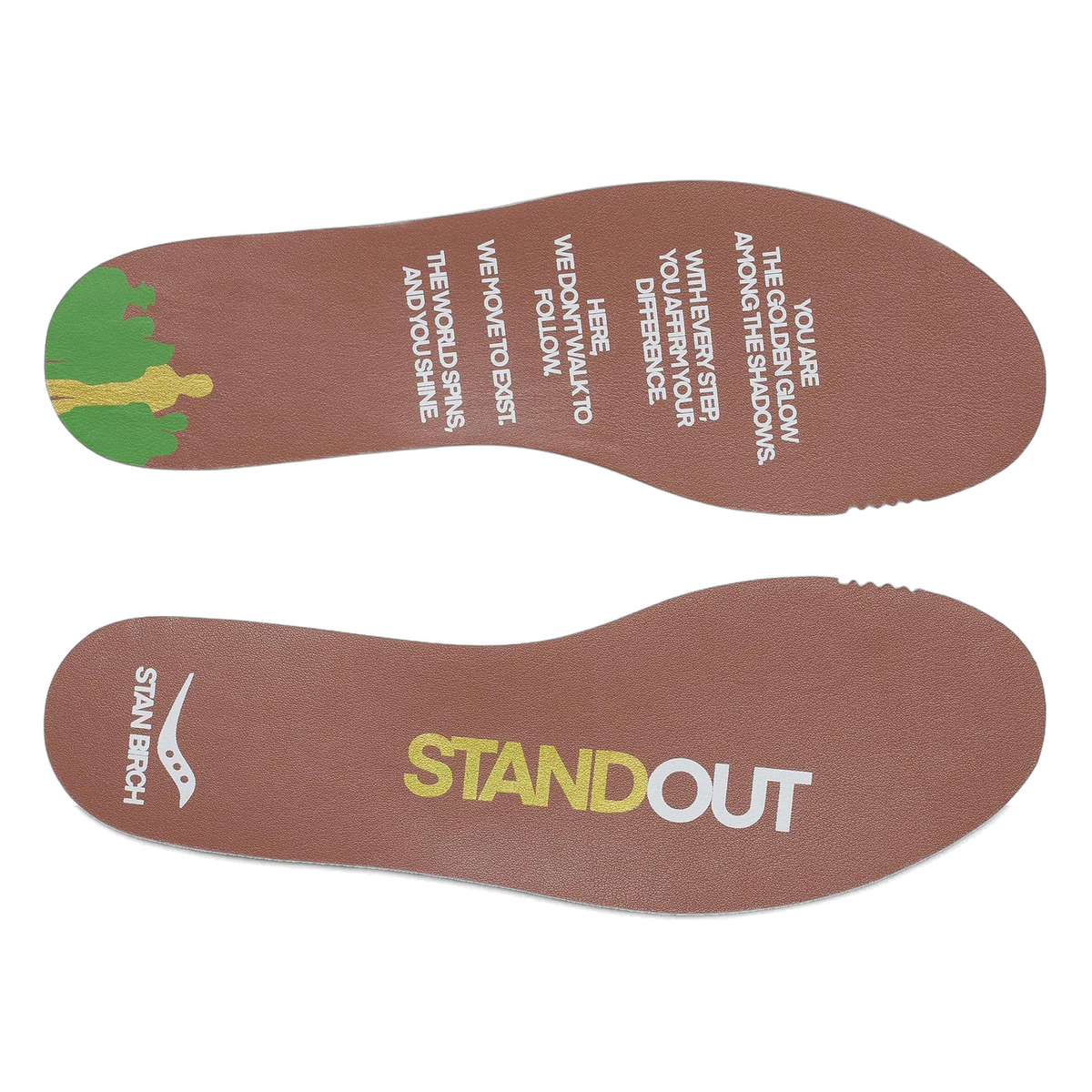 Pair of removable brown insoles printed with a Saucony logo, 'Stan Birch' and 'Standout' text, a motivational quote, and a colorful tree graphic.