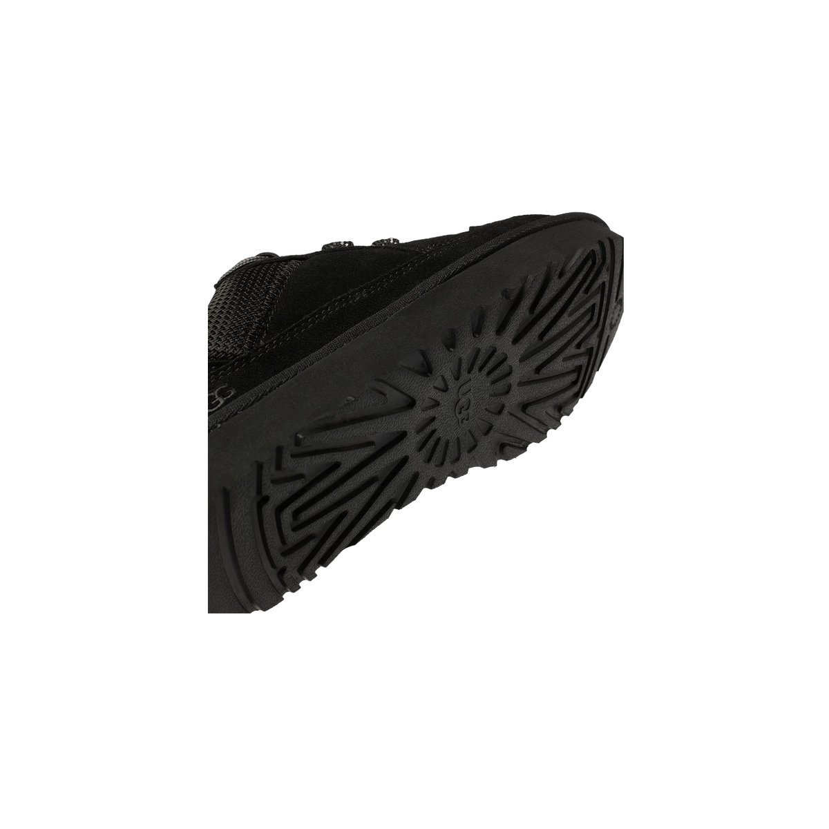 Close-up angled view of a black UGG shoe showing the treaded outsole with sunburst logo pattern and suede upper