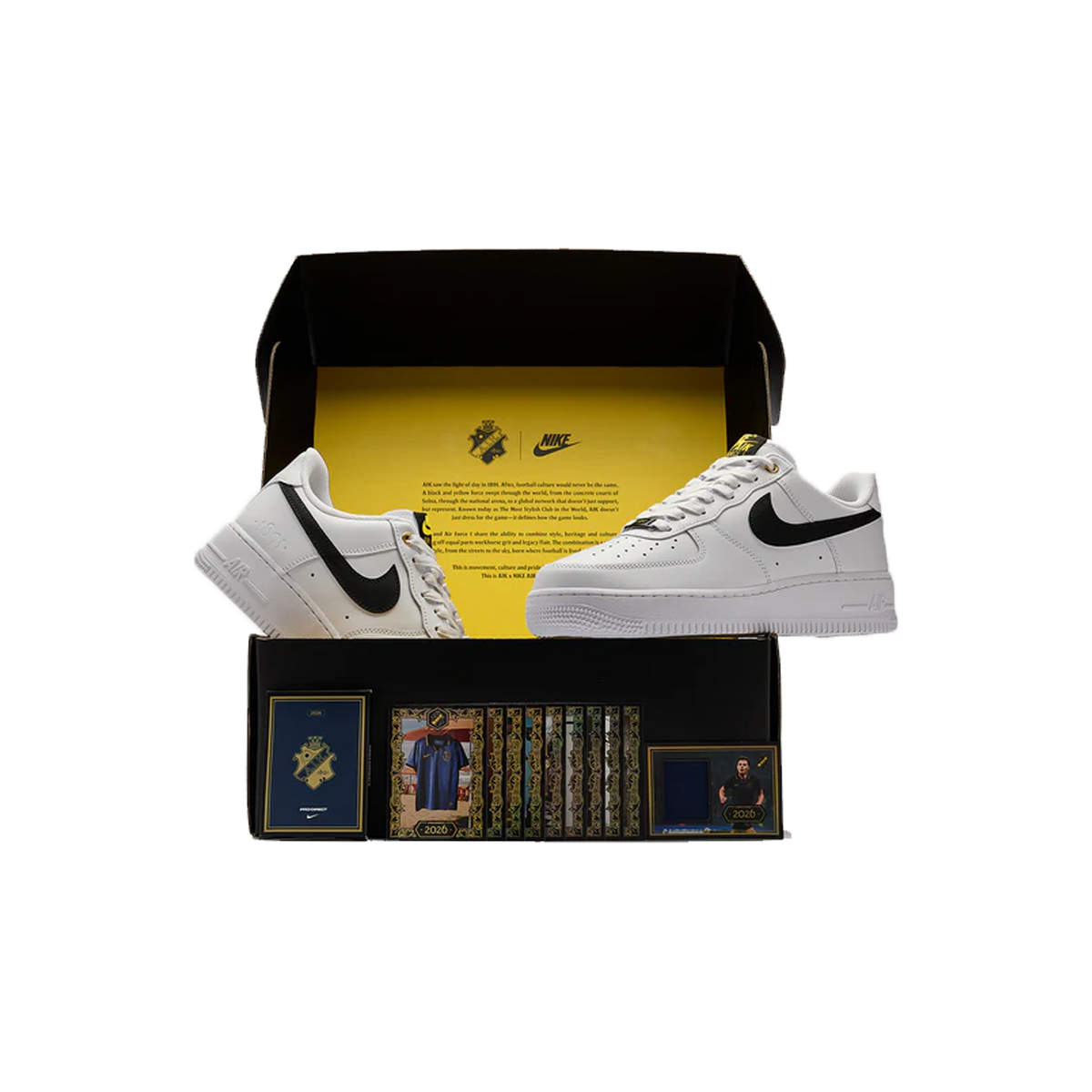 Un par de zapatillas Nike Air Force 1 Low blancas con swooshes negros, exhibidas dentro de una caja de marca negra y amarilla abierta junto a tarjetas coleccionables y folletos.