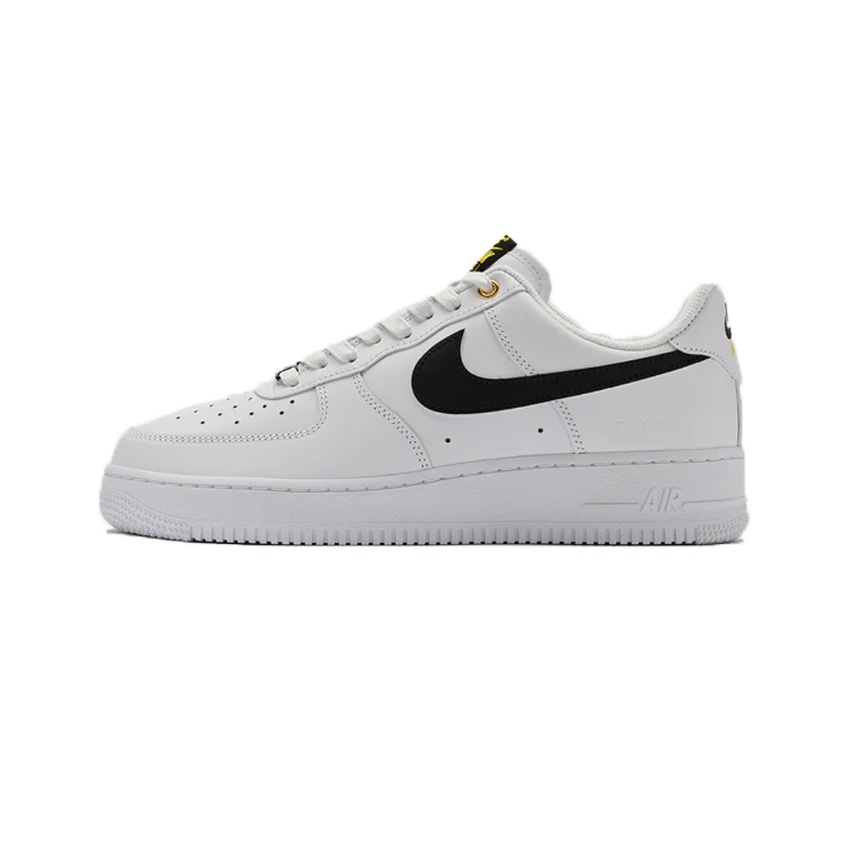 Vista lateral de una zapatilla Nike Air Force 1 Low blanca con swoosh negro, texto amarillo en el tirador y un pequeño parche gráfico cerca del talón.