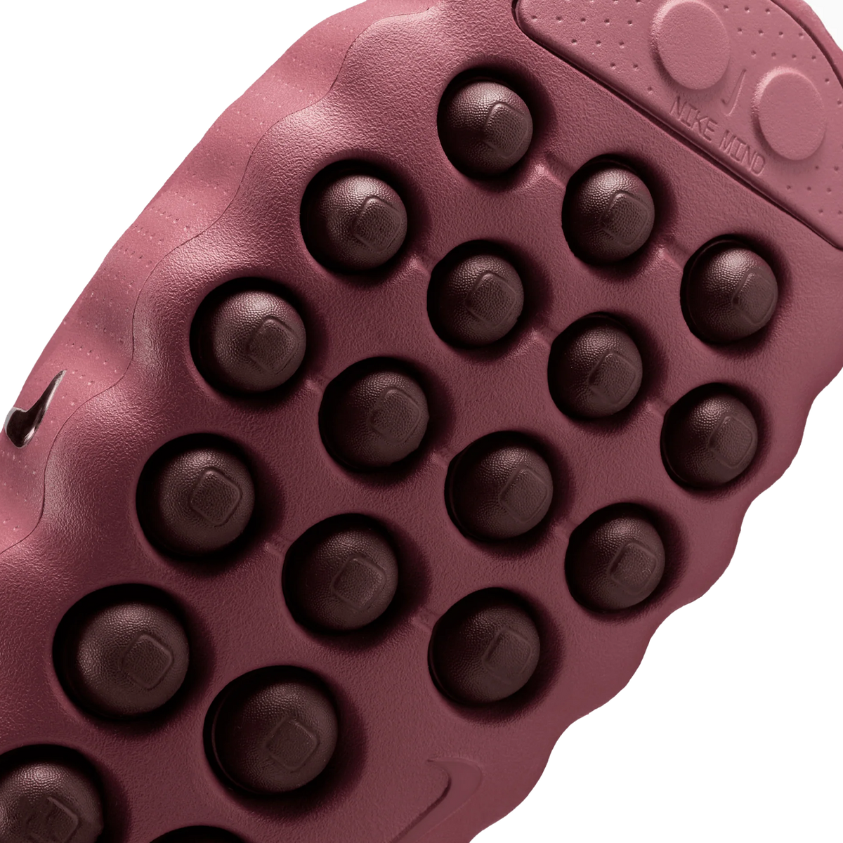 Nærbillede af den strukturerede yderåde på en rosa Nike Mind 001 sko med rækker af mørke runde gummiknopper og et lille Nike swoosh-logo på siden.