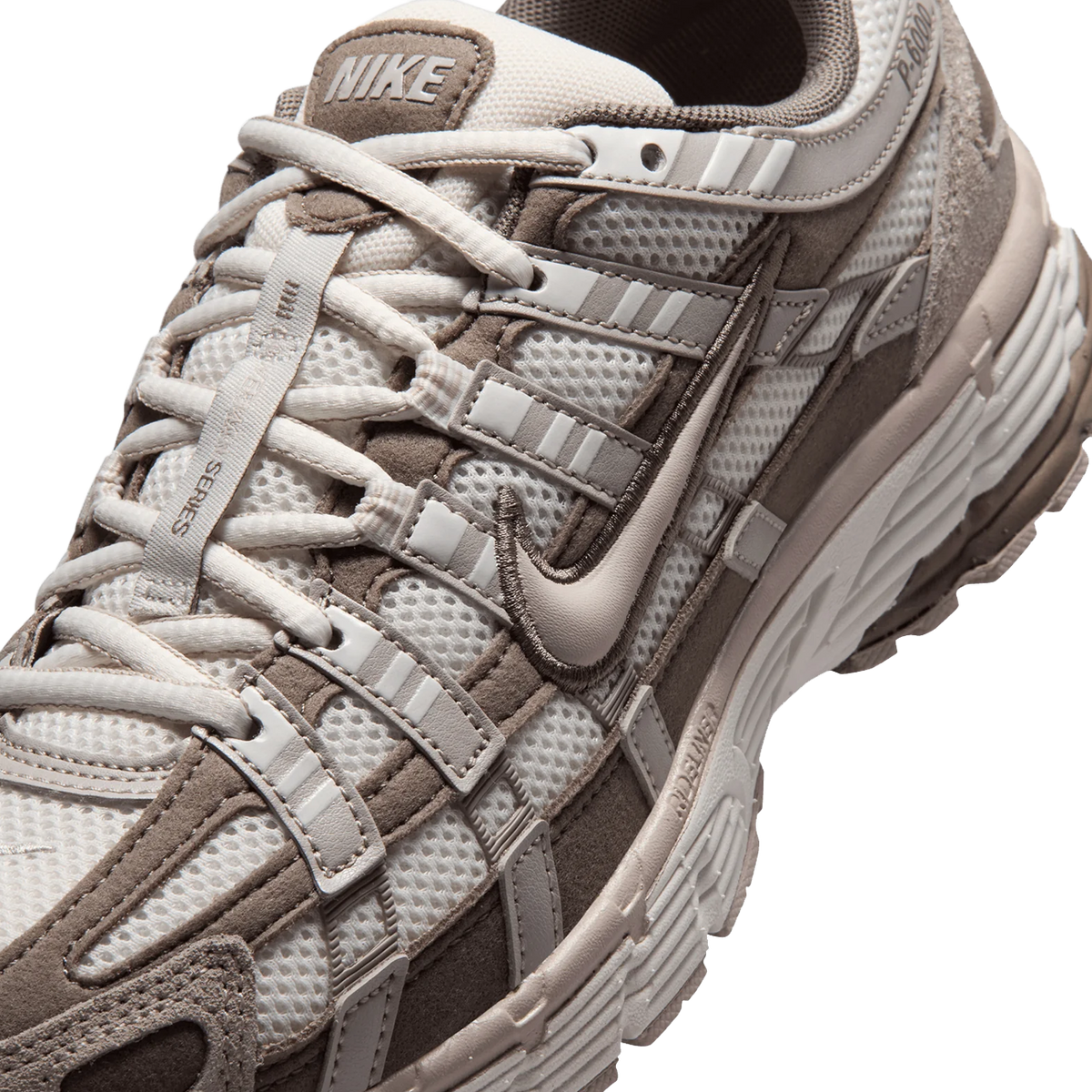 Close-up view of a Nike P-6000 sneaker toe box showing mesh fabric, suede overlays, layered Swoosh logo, and laces in taupe and cream tones.